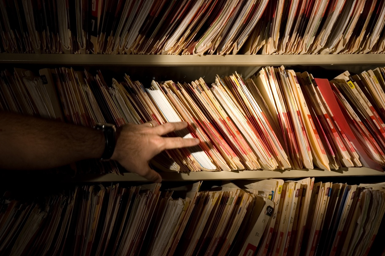 A man in front of a bookshelf of medical records