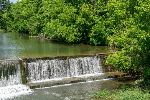 Man-made small waterfall in a river, low-head dam and trees